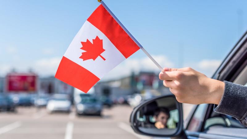 Person holding miniature canadian flag outside vehicle window