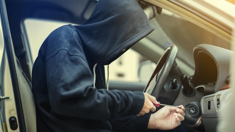 Side view of car thief using screwdriver to start car ignition.
